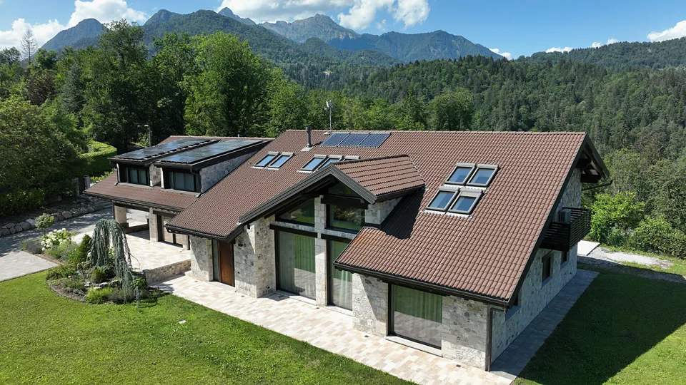 Casa in pietra con tetto bruno, abbaini con pannelli solari, terrazza e prato, vista dal drone